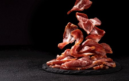Pile of cooked bacon on a slate plate against black background